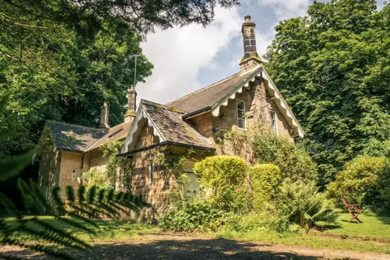 A charming stone cottage surrounded by lush green trees and plants.